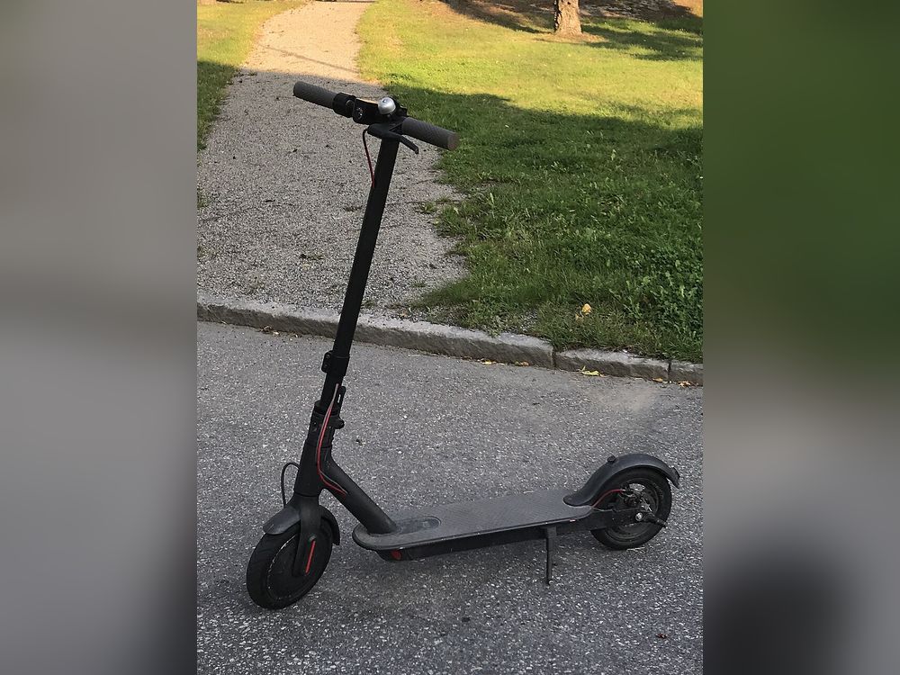 A black folding e-scooter standing on a footpath beside a lawn